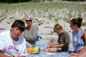 People on a blanket eating, on a sandy beach.