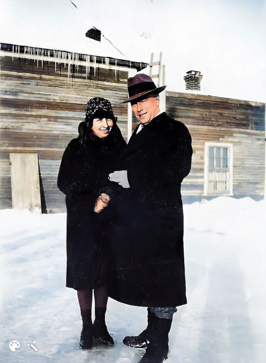 A man and woman posing outside dressed in black coats and hats.