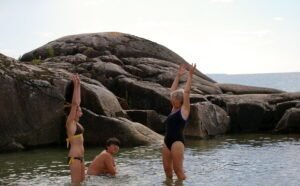 People in the water one sitting and two standing with their arms up and laughing.