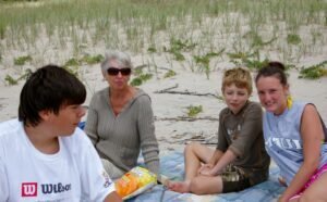 People sitting on a blanket on a sandy beach eating.