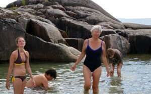 A woman standing in water with two others exploring the water while seated