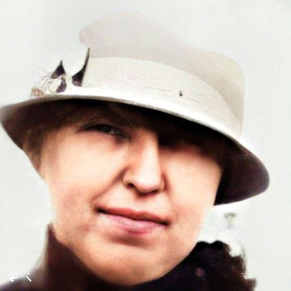 A headshot of a women wearing off white cloche hat with a ribbon above brim.