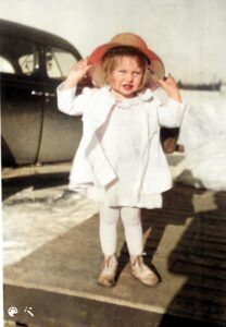 A childe with a red hat on. She is holding the brim with both her hands.